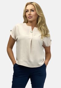 Jasnoróżowa bluzka krótki rękaw z okrągłym dekoltem, detalami w postaci fałd oraz srebrnymi guzikami na rękawach. Gładki, textured materiał.