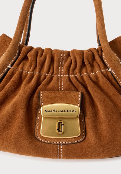 Pruun seemisnahast käekott kogutud disainiga, kuldsete detailide ja õmmeldud aktsentidega. Lukul on nähtav brändi logo.