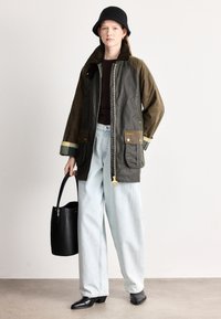 Καφέ και ελαιδί αδιάβροχο μπουφάν με φερμουάρ στο μπροστινό μέρος, δύο μπροστινές τσέπες και χρυσά κουμπώματα. Φορεμένο με ανοιχτόχρωμο τζιν και μαύρες μπότες με τακούνι.