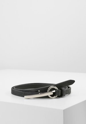 Cinturón de cuero negro con hebilla circular plateada y cierre delgado de metal, enrollado sobre una superficie blanca contra un fondo liso.