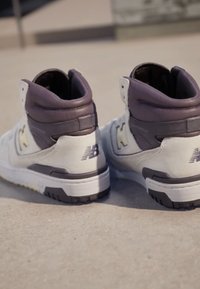 Wysokie trampki w jasnoszarym i ciemnopurpurowym skórze i tkaninie. Posiadają gumową podeszwę oraz wyraźne logo "N" po bokach.