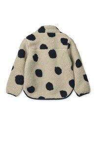 Fleecejakke i beige med store sorte polkaprikker. Har rundet kant, høj krave og en baglomme. Blød tekstur og afslappet design.