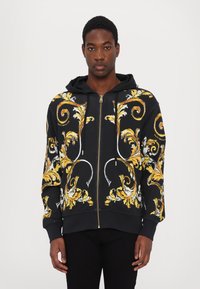Felpa nera con zip, caratterizzata da motivi floreali gialli e bianchi, realizzata in misto cotone, con cappuccio regolabile con cordino e polsini a coste.