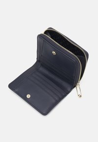 Portafoglio in pelle blu navy con zip dorata, multiple fessure per carte e chiusura a bottone. L'interno presenta una fodera a motivo.