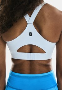 Bra sportivo bianco con design a racerback, caratterizzato da un dettaglio a taglio e chiusura con gancio, abbinato a pantaloni atletici blu.