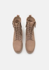 Botines beige con una suave textura de gamuza, con cierre de cordones en la parte frontal y cremallera lateral, puntera redondeada y suela gruesa.