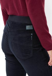 Donkerblauwe corduroy broek met een brede elastische tailleband, twee achterzakken, decoratieve stiksels en een gestructureerd label op de tailleband.