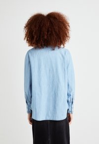 Lyseblå denimskjorte med lange ermer, knappmansjetter og rundet kant. Har en myk tekstur og et enkelt, klassisk design.