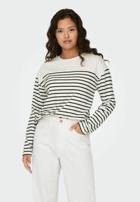 Langærmet top i creme med sorte vandrette striber; rund halsudskæring, blødt stof, afslappet pasform. Sammen med højtaljede hvide jeans.