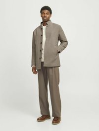 Grå uld-blandingsfrakke med høj krave, sorte knapper og sidelommer. Kombineret med beige bukser og brune snørebåndssko.