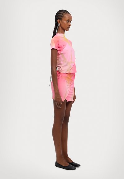 Haut rose à manches courtes associé à une mini-jupe assortie, fabriqué dans un tissu léger et lisse avec un design dégradé subtil.
