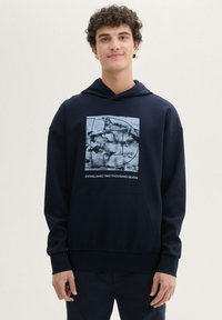 Granatowa bluza z kapturem z nadrukiem z przodu w jasnym niebieskim i czarnym kolorze. Posiada kieszeń typu kangur, ściągacze w mankietach oraz luźny krój.