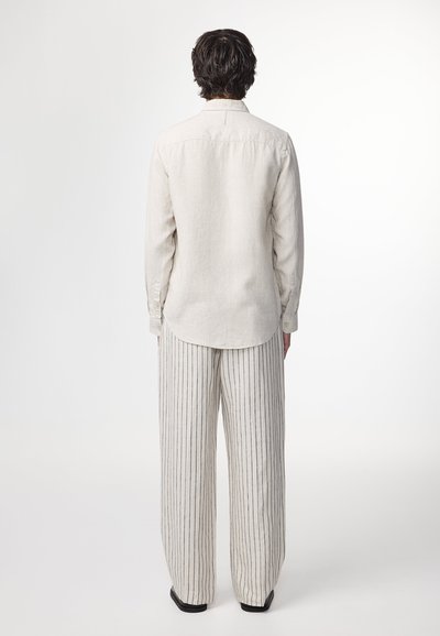 Lys beige linned skjorte med en knap-ned krave, parret med brede bukser med lodrette striber i lyse og mørke nuancer.