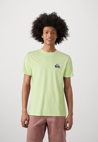 Light green cotton t-shirt with short sleeves, featuring a small navy logo on the chest. Smooth texture, crew neck design.