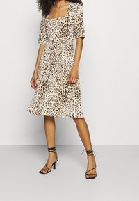 Leopardmönstrad klänning med fyrkantig halsringning, korta ärmar, åtsittande midja och böljande kjol. Bärs med svarta smala högklackade sandaler.