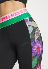 Czarne legginsy z żywym kwiatowym wzorem po boku oraz różowym i zielonym pasem w talii z logo Nike.