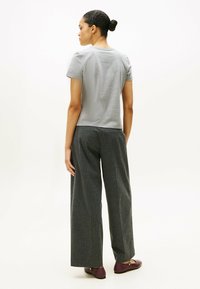 Grå kortærmet t-shirt parret med brede ben, mørkt stribede bukser. Modellen har burgunder flade sko på. Enkel, afslappet pasform design.