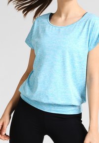Camiseta de mezcla azul claro con cuello redondo, mangas cortas y un ajuste relajado, combinada con leggings negros ajustados.