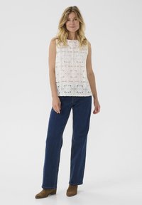 White sleeveless top with floral eyelet design, paired with dark blue straight-leg jeans and brown suede ankle boots.