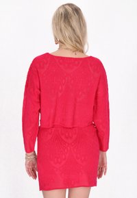 Rosa virkad klänning med långa ärmar, som har ett dekorativt mönster och en något cropped design vid midjan, med en texturerad finish.