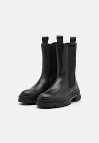 Černé kožené kotníkové boty s elastickými bočními panely, strukturovaným svrškem a robustní gumovou podrážkou pro lepší trakci. Obsahují poutka pro snadné obouvání.