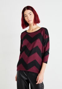 Burgunder- und schwarzes Langarmoberteil mit einem Chevron-Muster. Weicher Stoff mit einem entspannten Halsausschnitt und einer leicht übergroßen Passform.