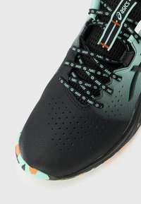 Black and teal ASICS padel shoe with patterned laces and perforated toe on a white background.
