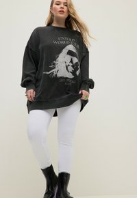 Överdimensionerad svart sweatshirt med vit grafisk tryck, kombinerad med vita leggings och svarta ankelboots. Slät tyg, avslappnad passform.