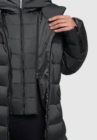 Puffjakke i sort med en quiltet tekstur; har dobbelte lynlåse og sidelommer. Hætte design med en glat inderside.
