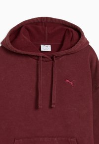 Bordeaux hættetrøje lavet af blødt stof, med en kængurulomme, snørrelse på hætten og et lille lyserødt Puma-logo på brystet.