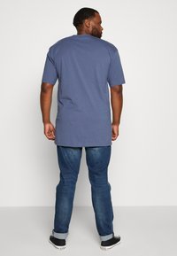 Blå T-skjorte med korte ermer, rund halsutskjæring, avslappet passform, laget av bomull, kombinert med denimjeans og svarte treningssko med hvite såler.