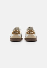 Hvite sneakers med beige og brune detaljer, semsket hælpaneler, og "VEJA"-logo i hvitt. Teksturrubber såle med markant mønster.