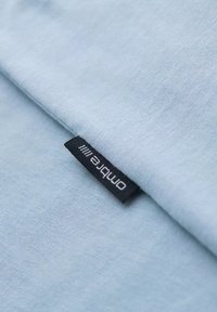 Světle modrá látka s jemnou texturou, se černou etiketou s nápisem "omplete", umístěnou na okraji.