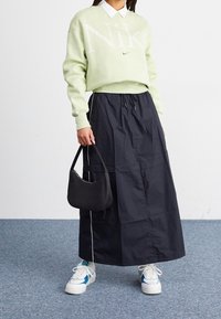 Light green sweater with large "Nike" logo, paired with a black, mid-length skirt. Accessories include a small black bag and white sneakers with blue accents.