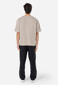 Tricou dungi bej deschis, cu un croi lejer, mâneci scurte și guler rotund, asortat cu pantaloni negri și pantofi albi.