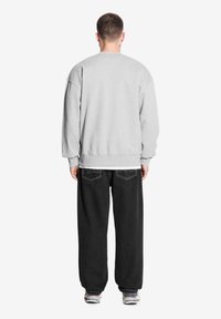 Szara sweatshirt z opadłymi ramionami, prążkowanymi mankietami i dołem, w połączeniu z luźnymi czarnymi dżinsami z przeszyciami na tylnych kieszeniach i trampkami.