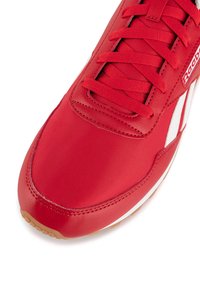 Scarpa da corsa rossa con tomaia in tessuto liscio e suola in gomma. Dettagli bianchi e lacci aggiungono contrasto al design snello.
