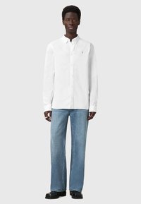 Camicia bianca a maniche lunghe con colletto button-down, abbinata a jeans in denim azzurro chiaro a gamba larga. Design semplice senza motivi evidenti.