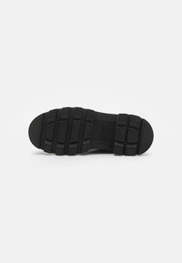 Zwarte sneakersole met textuur rubber, voorzien van een loopprofiel voor grip, een langwerpige vorm en een logo dat is ingedeukt nabij de hiel.