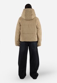 Kremzės spalvos kordurolio pūkinė striukė su gobtuvu, su horizontaliai siūtomis dalimis. Sukomplektuota su laisvai krentančiomis tamsiomis džinsinėmis kelnių.