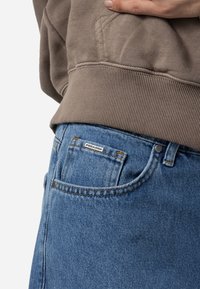 Bleka blå denimjeans med klassisk passform, som har orange sömmar, nitar och en märkesetikett på bakfickan.