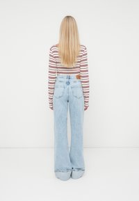 Ljusblå, vida jeans med hög midja, med en brun läderlapp på baksidan och en mjuk denimtextur. Randen långärmad topp.