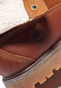Braune Lederstiefel mit einem beigen Fleece-Futter, wasserdichter Markenkennzeichnung und einer strukturierten, robusten Sohle mit ausgeprägtem Profilmuster.