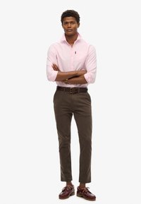 Jasnoróżowa koszula button-down, ciemnoniebieskie chinosy i burgundowe buty żeglarskie. Charakteryzuje się długimi rękawami, kieszenią na przodzie oraz brązowym paskiem.