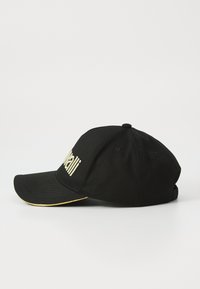 Boné de beisebol preto com texto em dourado bordado na frente e contorno dourado ao longo da borda da aba curva, repousando sobre uma superfície branca.