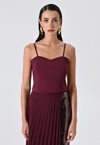 Top bordeaux senza maniche con scollatura a cuore, abbinato a una gonna plissettata con dettagli in paillettes su un lato.