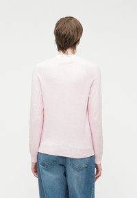 Maglione rosa chiaro, texture, con maniche lunghe e scollo rotondo, abbinato a jeans di denim a vita alta. Design semplice e minimale.