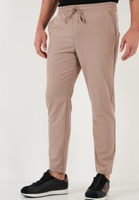 Beige joggerbroeken met elastische tailleband en trekkoord, zijzakken, slim fit, gecombineerd met zwart-witte sneakers.
