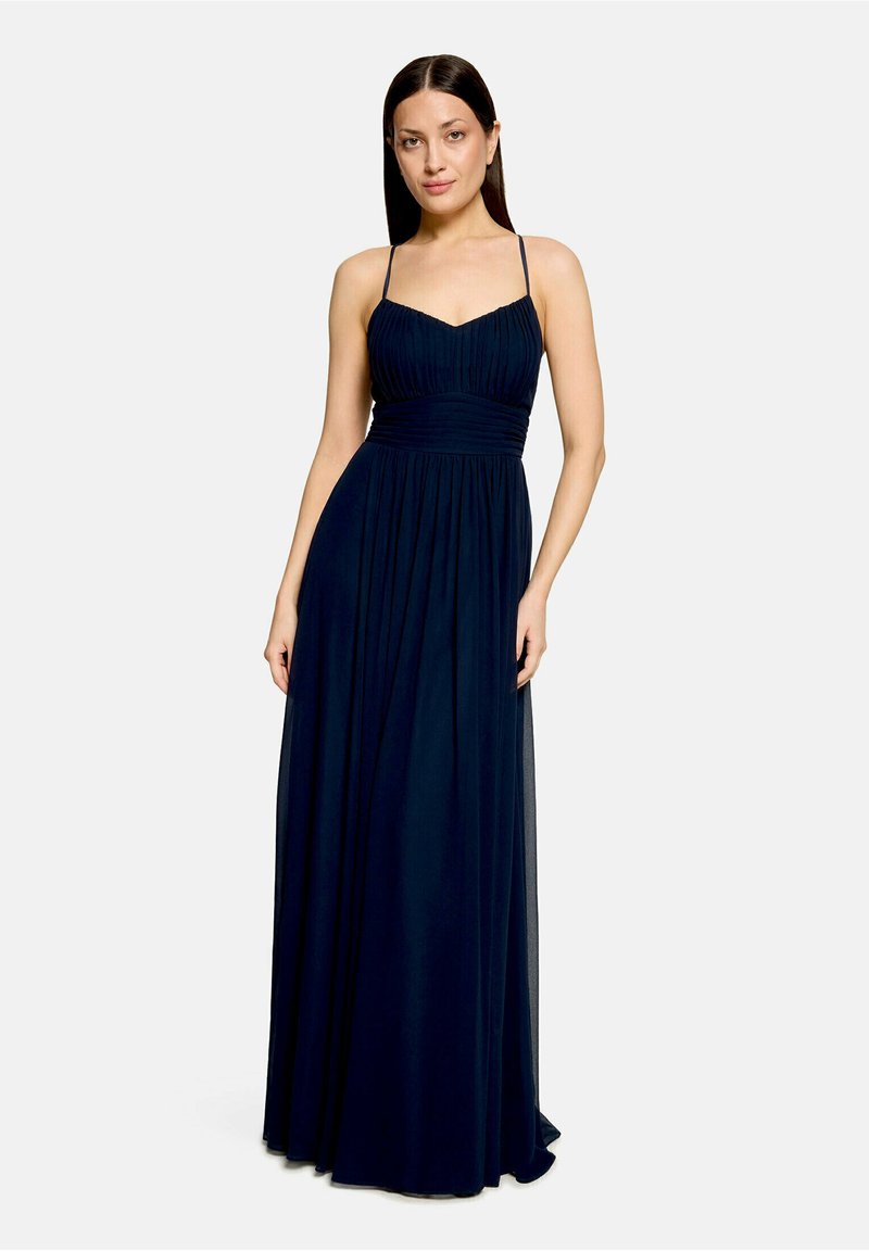 Femme aux cheveux lisses et foncés portant une robe longue bleu marine sans manches avec de fines bretelles et un corsage froncé.