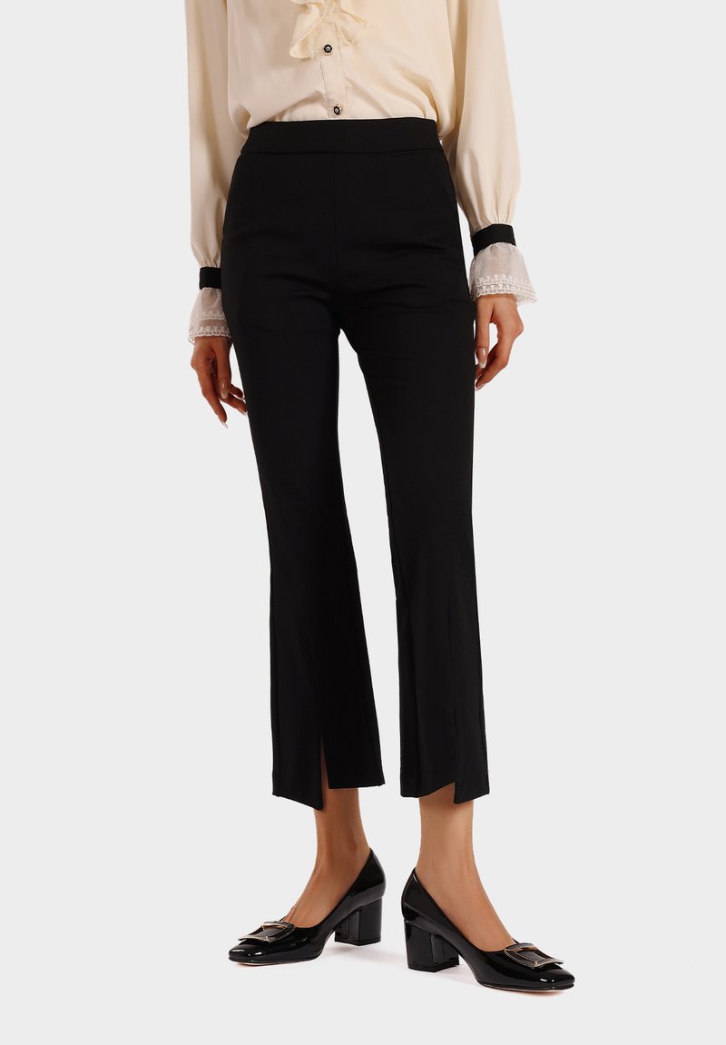 Pantaloni neri aderenti con fondo svasato e spacchi laterali, realizzati in un tessuto morbido. Abbinati a scarpe nere con tacco di blocco.